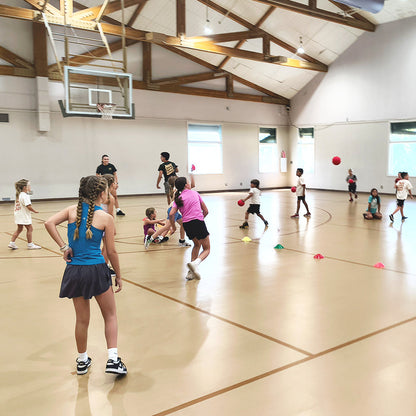 Children playing basketball in a gymnasium with coaches and sports balls on the court.